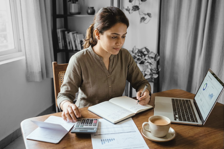 An Indian woman reviewing financial documents, a bank passbook and investment papers at a table, representing financial literacy and the wealth generation gap.